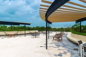 An outdoor patio with hexagonal patterned flooring, metal and wooden furniture, and a wooden pergola structure. - PH8C PANOR, Luxury Penthouse Alberca Privada (Tulum)