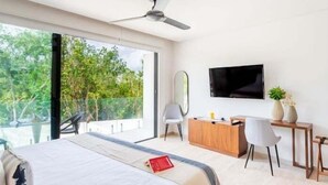 Een moderne slaapkamer met een bed, een bureau, een stoel, een televisie en een balkon met uitzicht op bomen.
