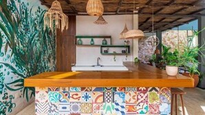 A kitchen with a wooden countertop, hanging wicker light fixtures, and a colorful tile backsplash.