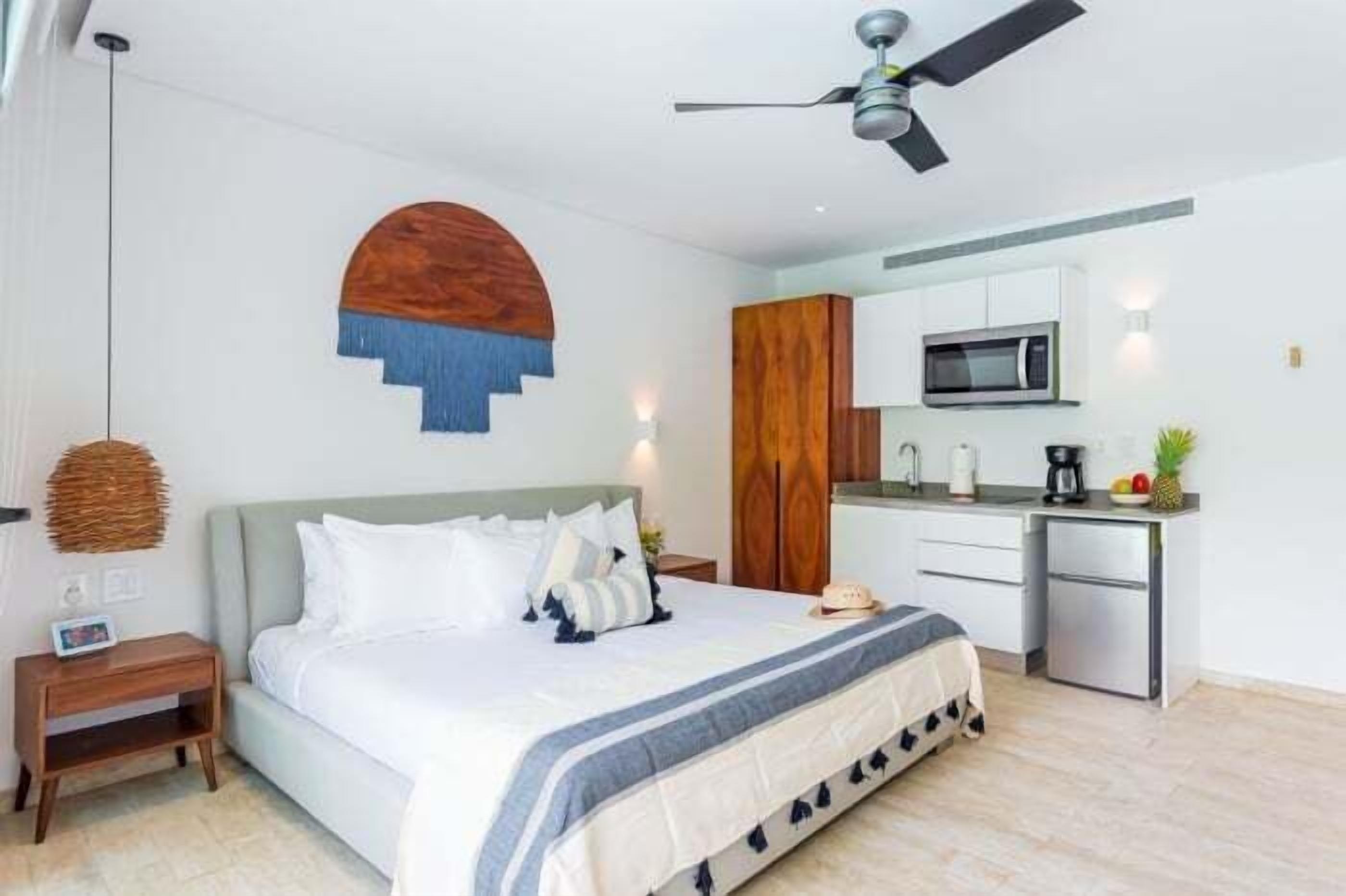 A bedroom with a bed, bedside table, and a small desk area with a microwave and sink.
