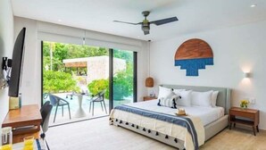 A modern bedroom with a bed, a ceiling fan, a TV, and a dining area with a table and chairs. - A102 CPL, Warm Swim Up Studio-2 (Tulum)