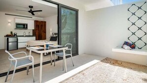 A modern kitchen with a microwave and cabinets, a dining area with a table and chairs, and a large sliding glass door leading to an outdoor patio. - A107 CPL, Magnifico Studio Garden Jungle View-2 (Tulum)