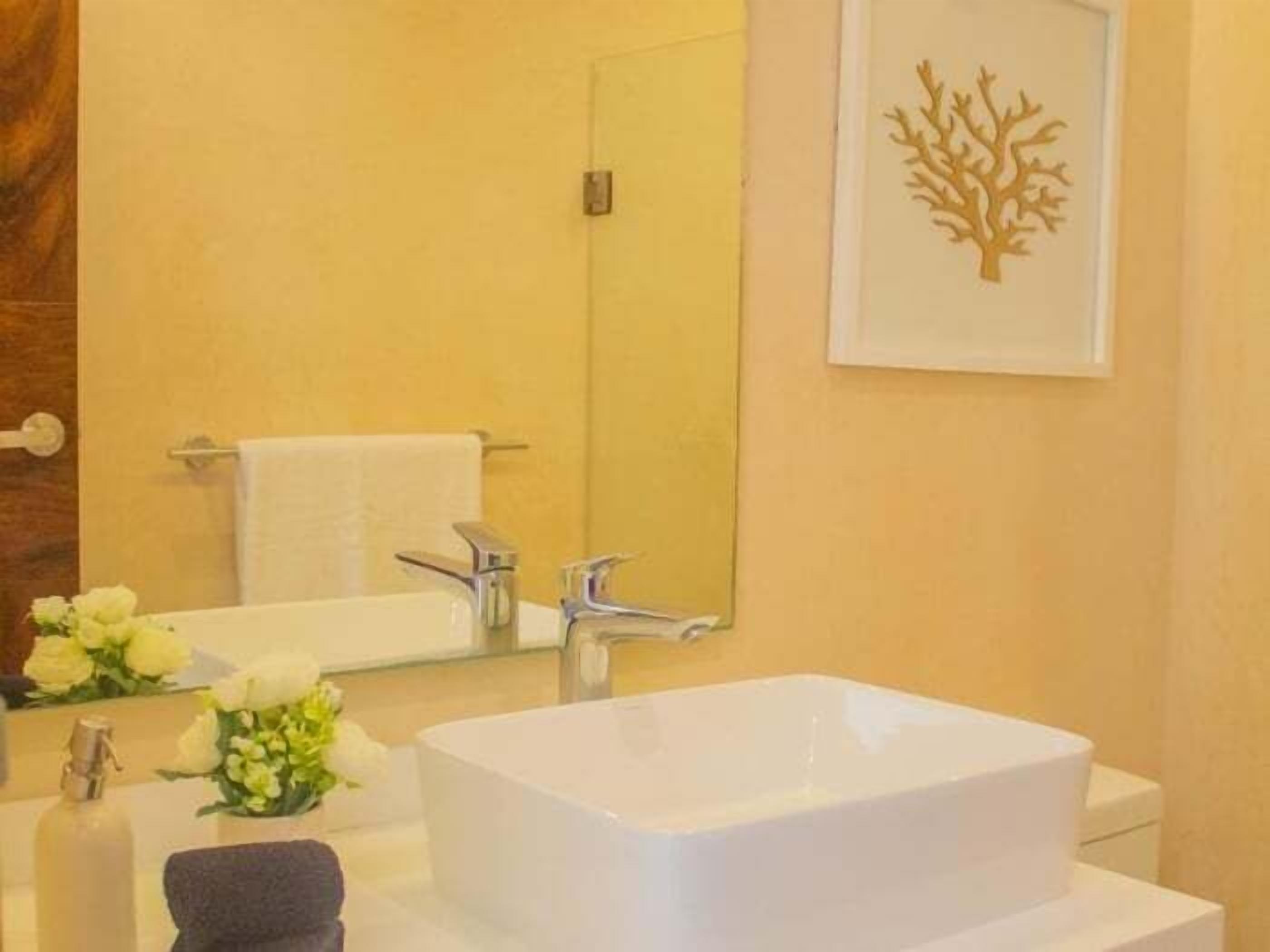 A bathroom with a white sink, a mirror, and a wall-mounted picture of a tree.