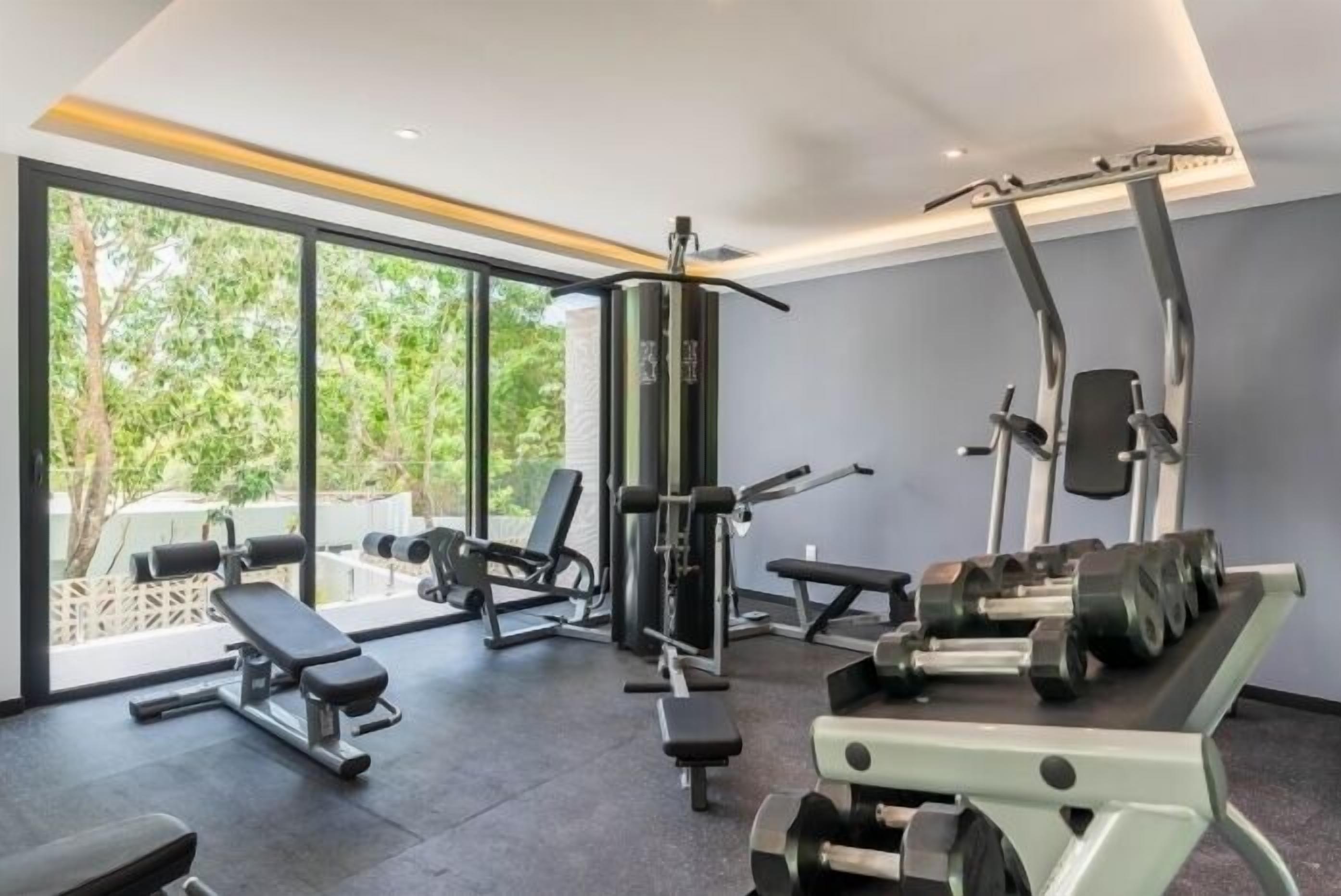 A gym with various exercise equipment, large windows, and a view of greenery outside.