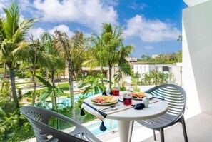 A dining area with a table set for two, overlooking a pool and lush greenery. - A210 CPL, Amazing Studio Lagoon View-2 (Tulum)
