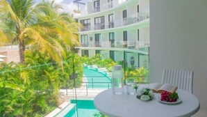 Un balcón con vista a una piscina, rodeado de exuberante vegetación y un edificio de varios pisos.
