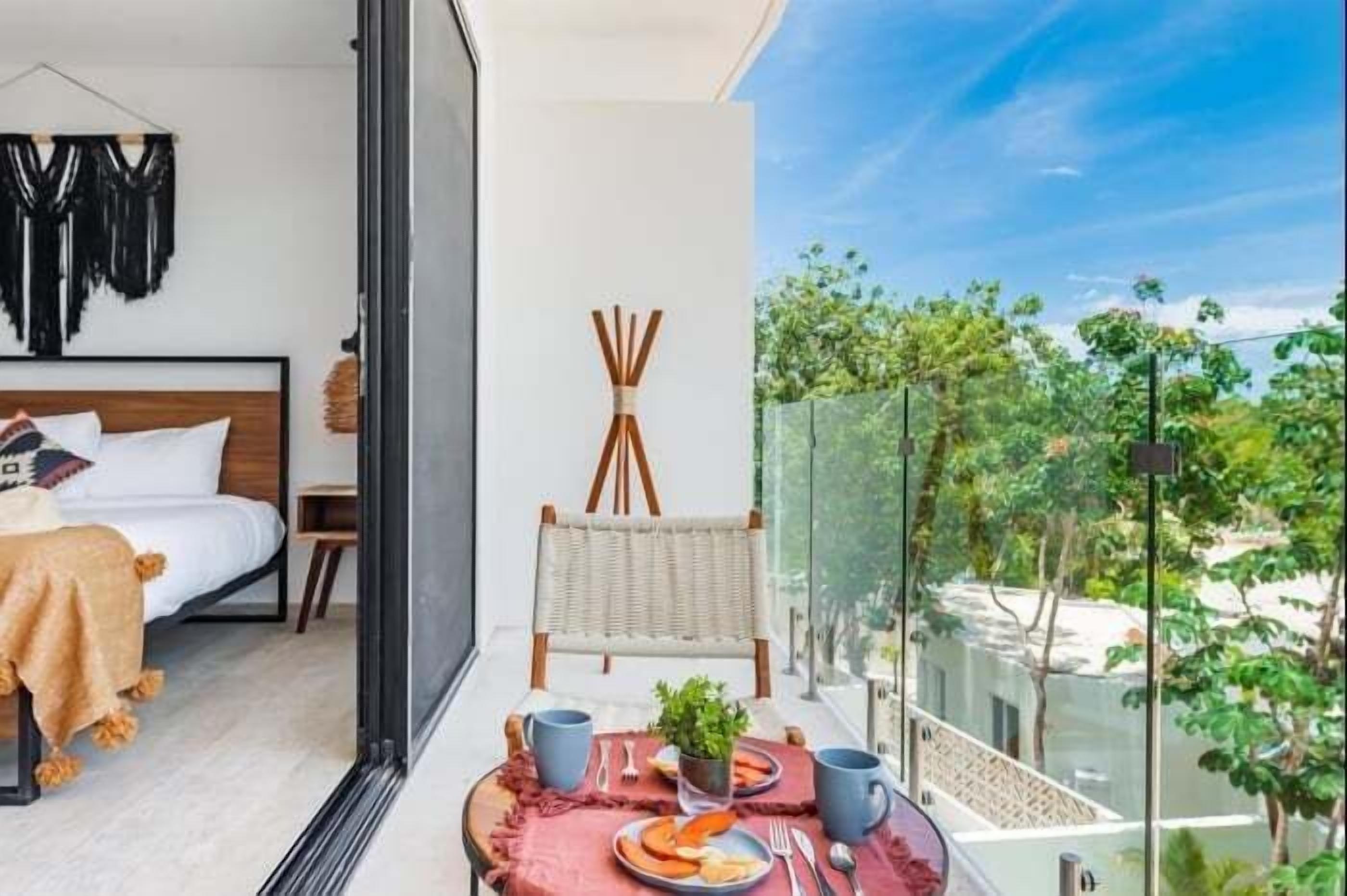 Un balcón con zona de comedor, una cama con cabecera y vistas a la vegetación.