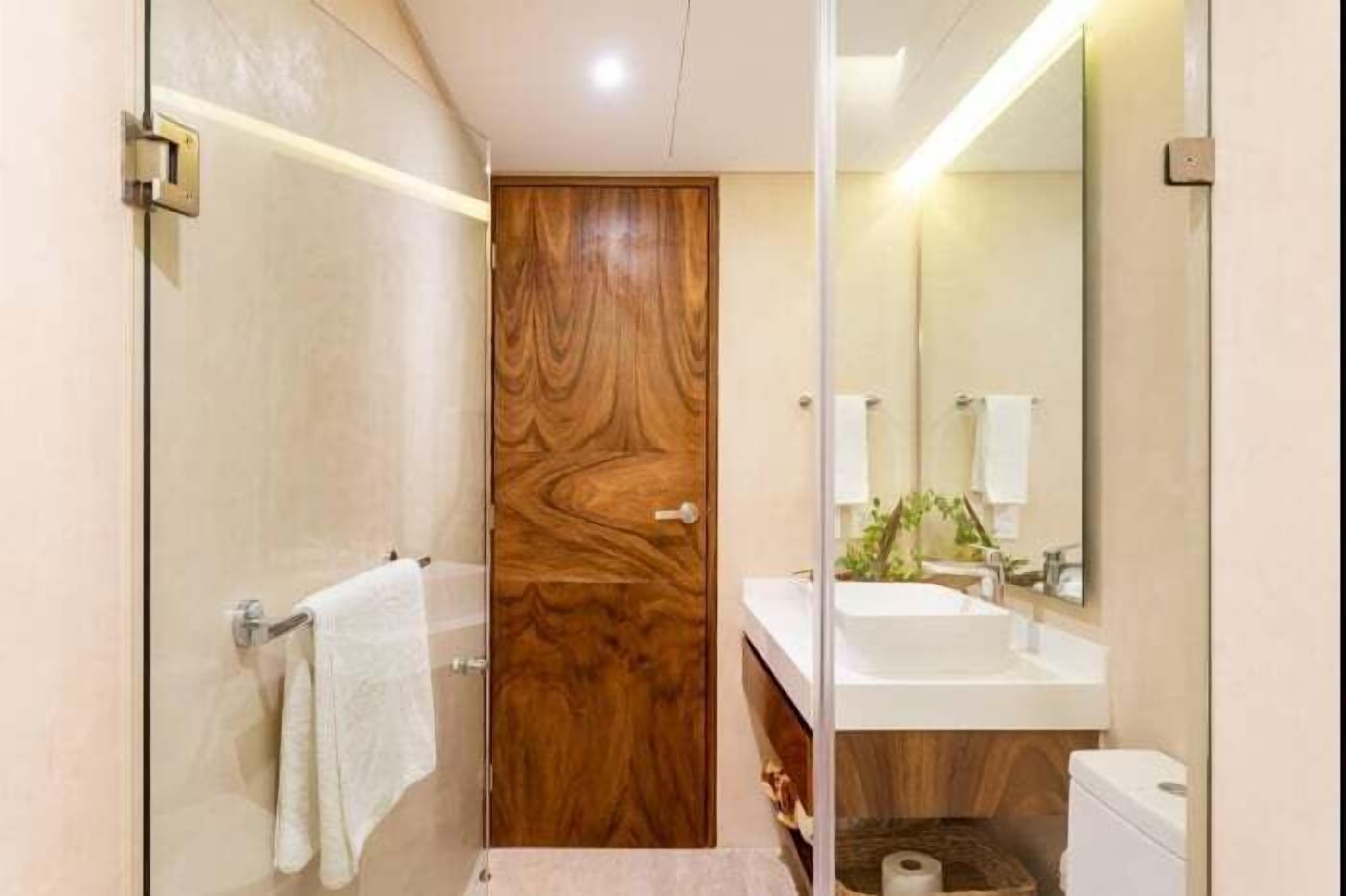 A modern bathroom with a wooden door, a glass shower enclosure, a white sink, and a mirror.