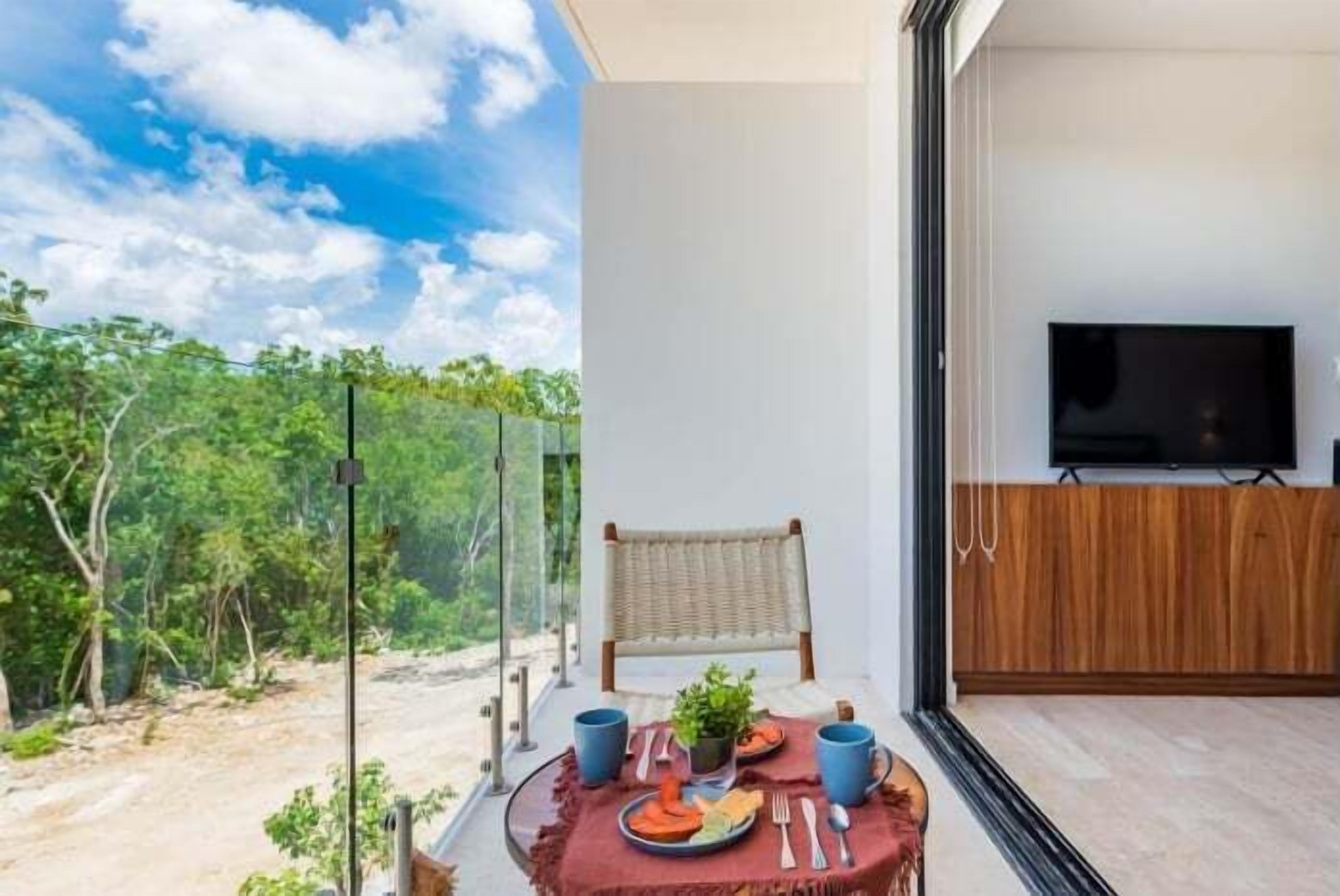 A room with a dining table set for two, a chair, a TV, and a view of the outdoors.