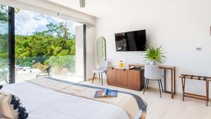 A modern bedroom with a large bed, a desk, a TV, and a balcony with a view of greenery. - B409 CPL, Studio Jungle View-No Air Conditioning-2 (Tulum)