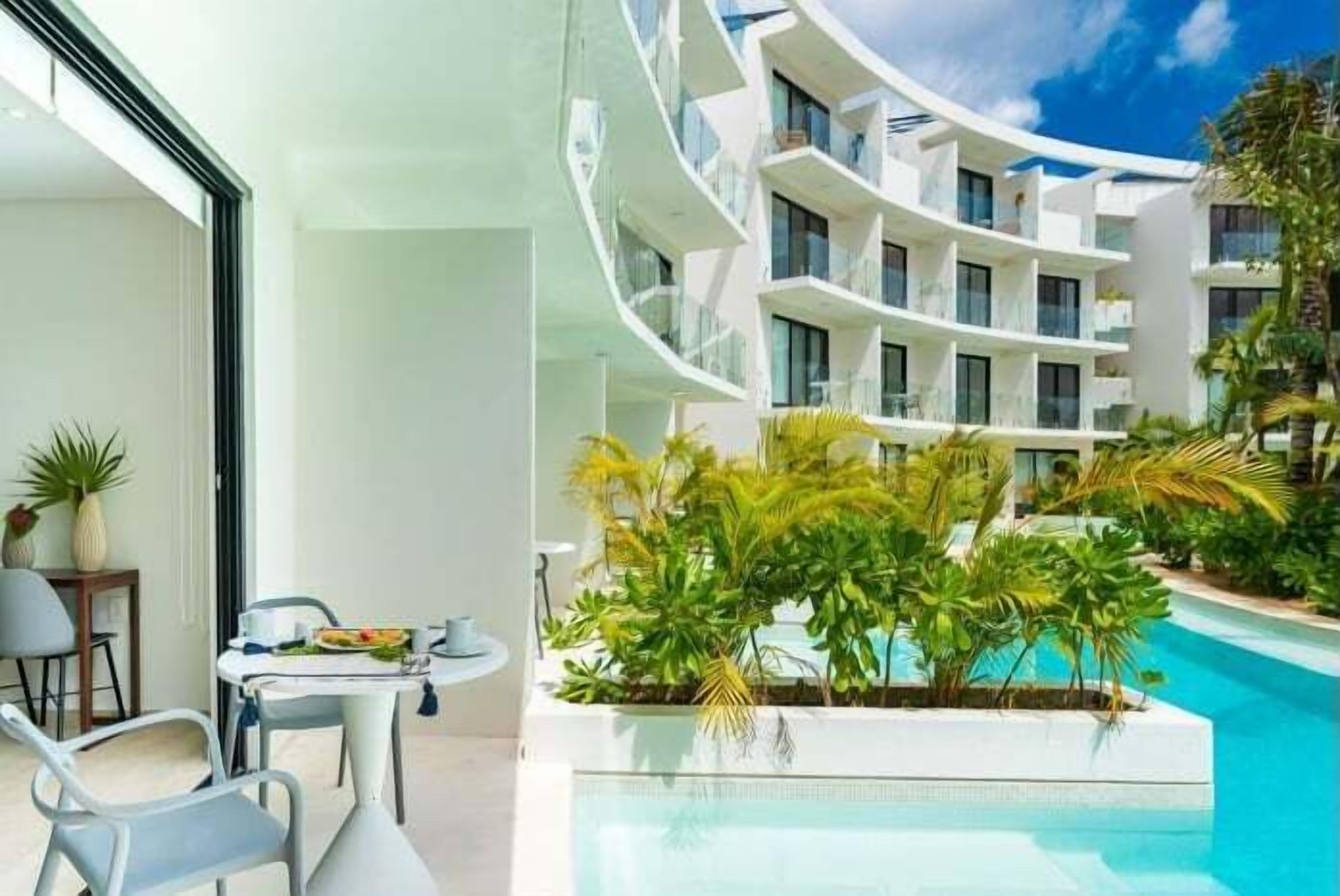 A modern hotel with a pool area, outdoor seating, and lush greenery.