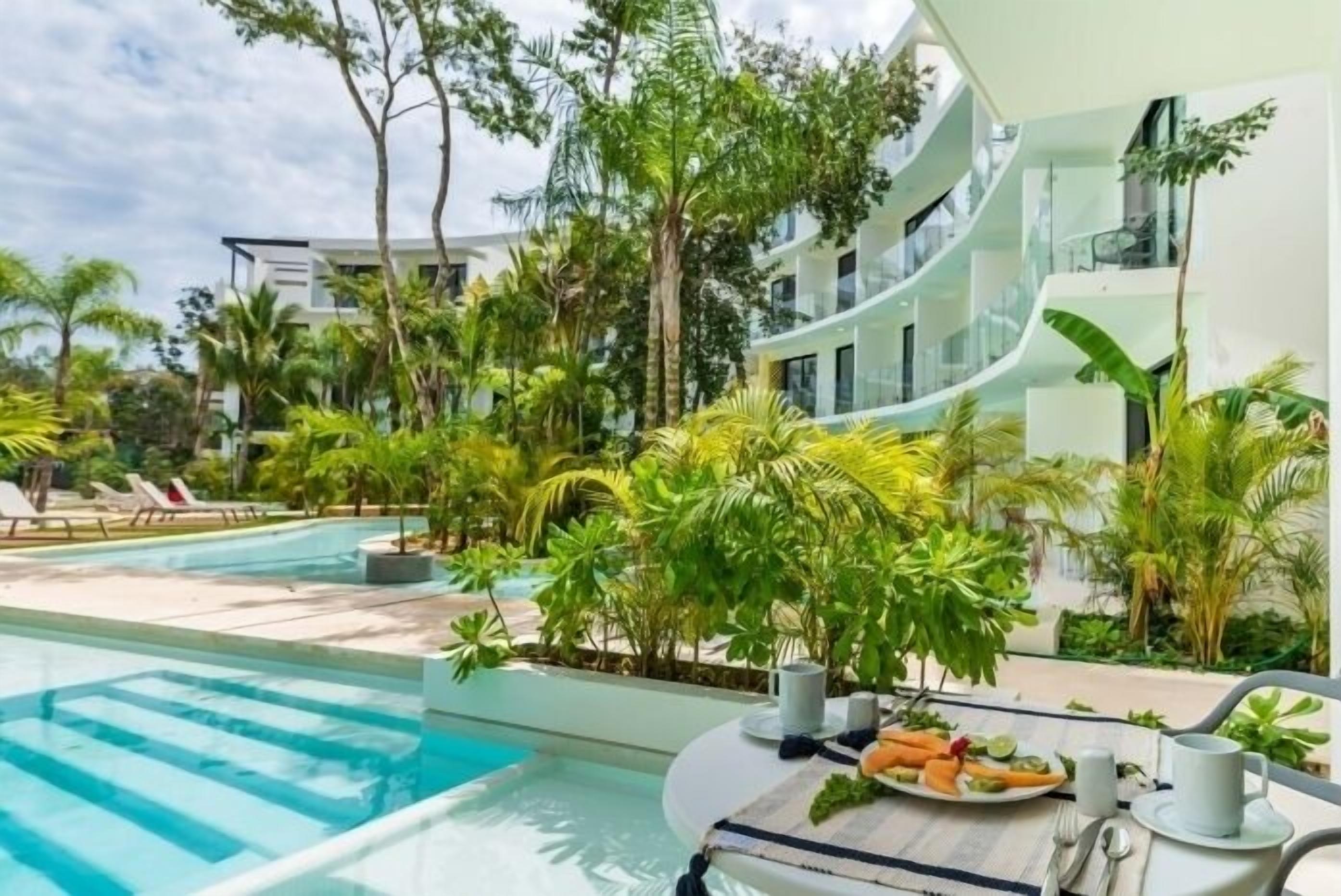 Un hotel moderno con piscina rodeada de exuberante vegetación y palmeras.