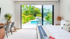Une chambre d’hôtel moderne dotée d’un grand lit, d’un bureau avec des chaises et offrant une vue sur une piscine et la verdure environnante.