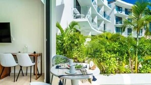 Quarto de hotel moderno com área de refeições, TV e varanda com vegetação exuberante.