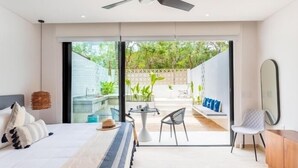 Een moderne slaapkamer met een bed, een plafondventilator, uitzicht op het buitenterras en een eethoek met stoelen en een tafel.