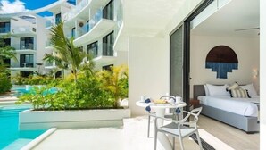 A modern hotel room with a balcony, a pool, and a view of the building's exterior. - D104 CPL, Grandioso 2 bedrooms swim up-2 (Tulum)