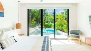 A modern hotel room with a large bed, a ceiling fan, and a view of a swimming pool and greenery. - D104 CPL, Grandioso 2 bedrooms swim up-2 (Tulum)