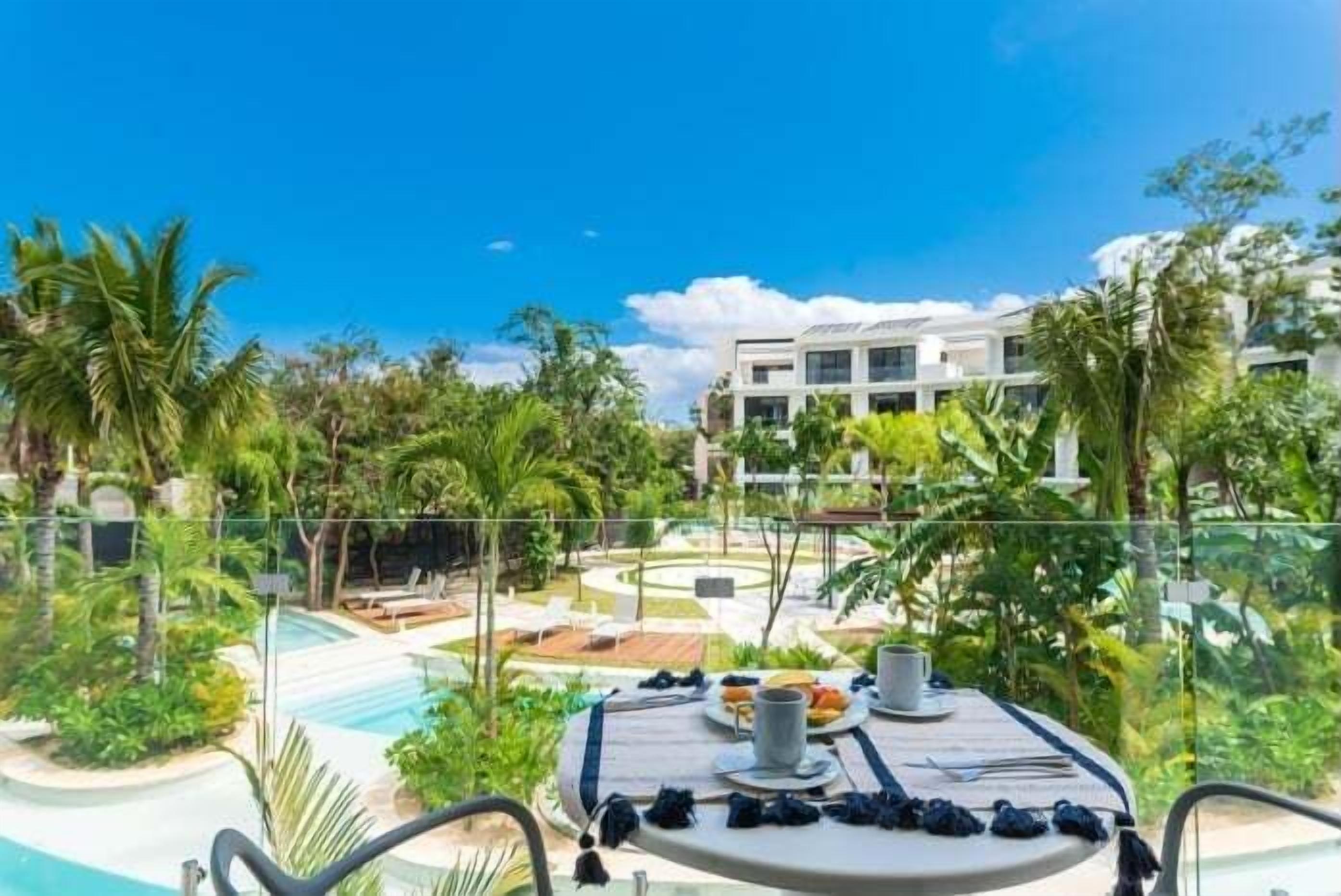 A poolside dining area with a table set for two, overlooking a pool and lush greenery.