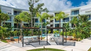 Et moderne hotel med poolområde, udendørs siddepladser og frodig beplantning.
