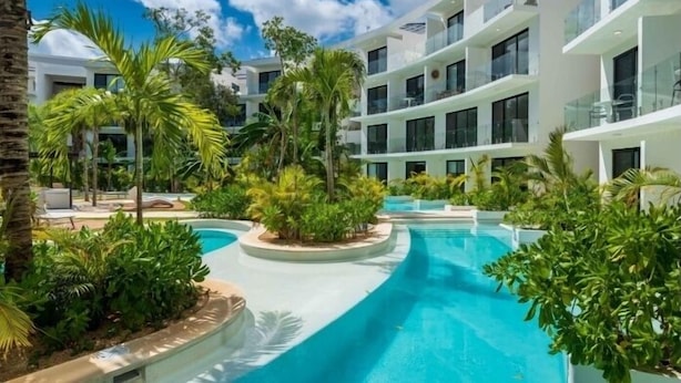 Et moderne hotel med en central swimmingpool, omgivet af frodig vegetation og palmer.