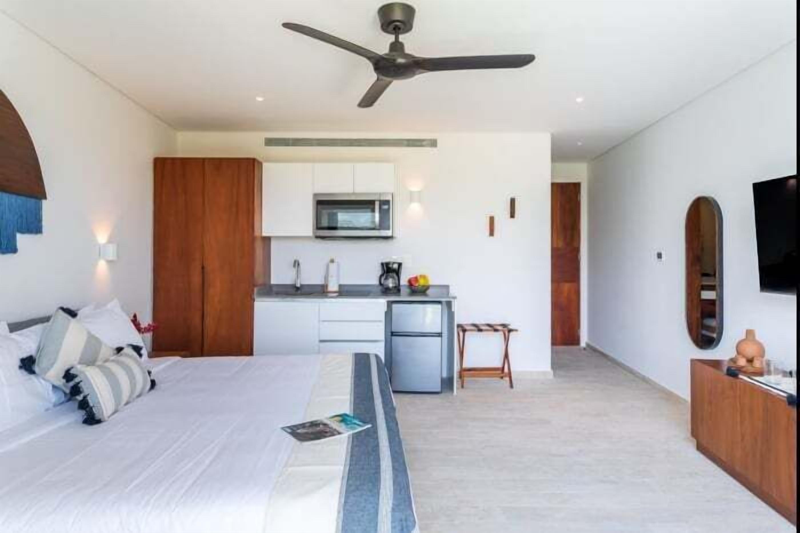 Een moderne hotelkamer met een bed, een kitchenette, een plafondventilator en een televisie aan de muur.