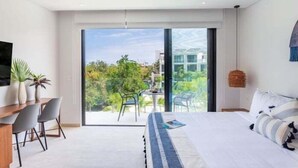 A modern hotel room with a large bed, a desk with chairs, a ceiling fan, and a view of greenery and buildings outside. - D302 CPL, Pleasant Studio Lagoon View-2 (Tulum)