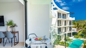 A modern balcony with a dining setup, a TV, and a view of a multi-story building and a pool. - D302 CPL, Pleasant Studio Lagoon View-2 (Tulum)