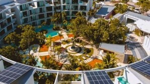 Et moderne hotel med en cirkulær pool omgivet af frodig vegetation og solpaneler på taget.