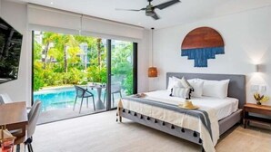 Ein modernes Schlafzimmer mit Bett, Deckenventilator, Blick auf einen Swimmingpool und einer Essecke mit Stühlen.