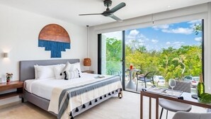 A modern bedroom with a large bed, a ceiling fan, and a view of greenery outside. - E203 CPL, Cowork /Gym/Estilo moderno / Jardín-2 (Tulum)