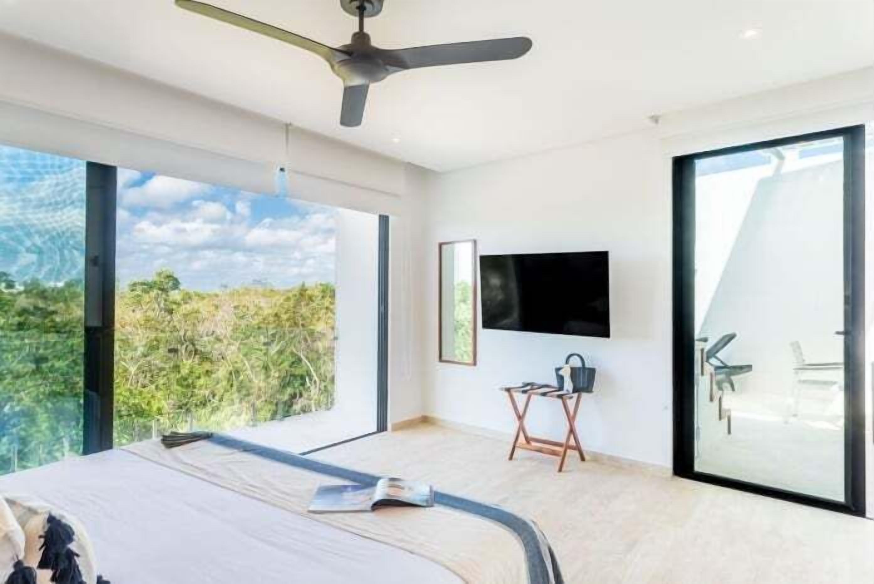 Quarto moderno com cama grande, ventilador de teto, televisão e porta de vidro deslizante para área externa.