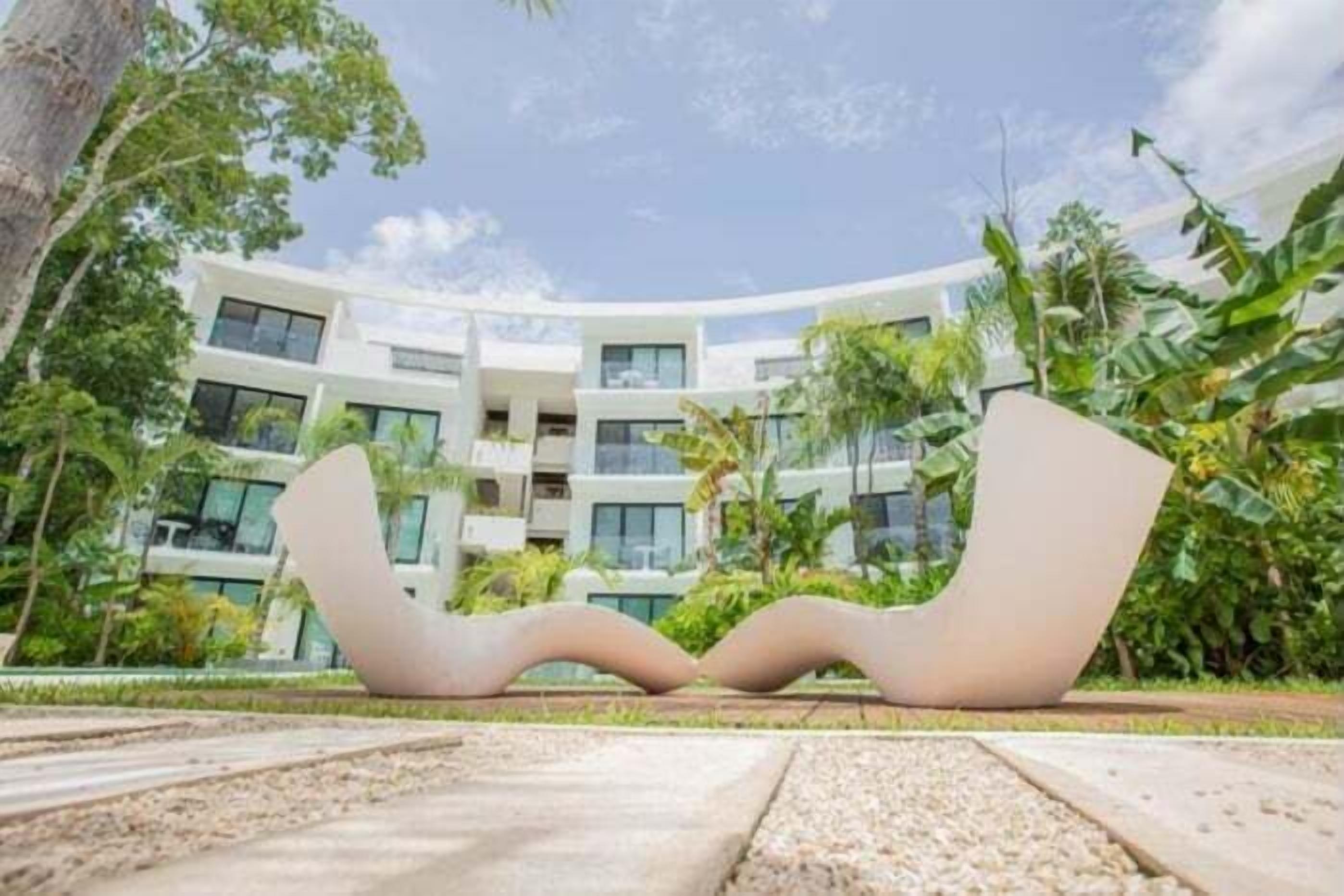 Een modern hotel met een gebogen gevel, grote ramen en een centraal gelegen tuin met een uniek kunstwerk.