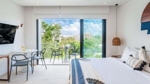 Ein modernes Hotelzimmer mit einem großen Bett, einem Schreibtisch mit Stühlen, einem Balkon mit Tisch und Stühlen sowie einem an der Wand befestigten Fernseher.