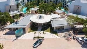 Ein modernes Hotel mit einem kreisförmigen Innenhof, mehreren Schwimmbecken und einem Parkplatz mit einigen Autos.