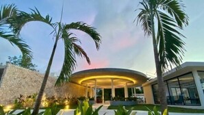 Un edificio moderno con una estructura central circular, rodeado por un jardín ajardinado con palmeras y diversas plantas.