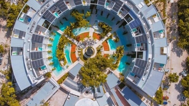 Un hotel circular con varios pisos, un patio central con piscina y abundante vegetación circundante.