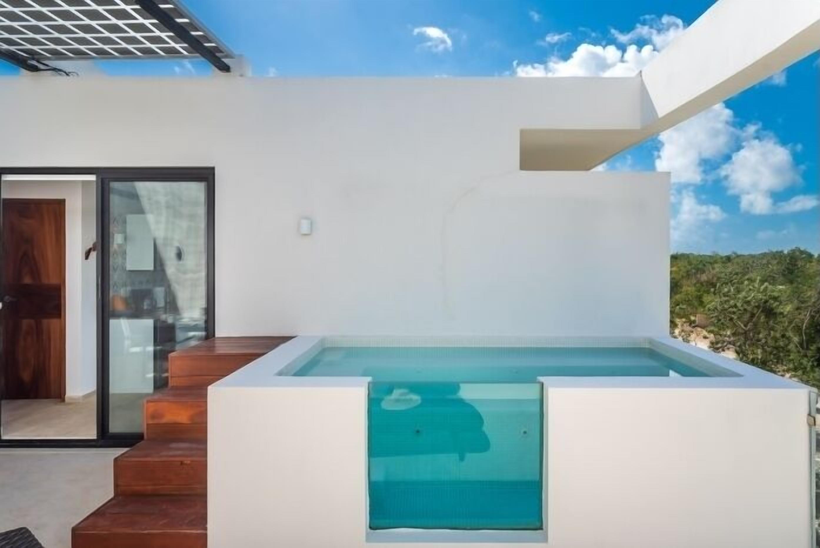 A modern outdoor pool area with a clear blue pool, wooden steps, and a glass door leading to a covered entrance.