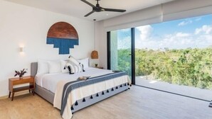 Un dormitorio moderno con una cama grande, un ventilador de techo, una mesita de noche y vistas a la vegetación a través de un ventanal corredero.