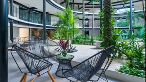 Un atrium intérieur moderne, conçu selon un plan circulaire, avec des chaises à structure métallique noire, une plante centrale et plusieurs niveaux dotés de balcons.