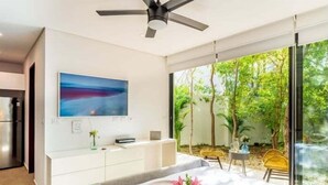 Une chambre moderne avec une grande fenêtre, un ventilateur de plafond, une table de chevet avec une assiette et des fleurs, et un tableau accroché au mur.