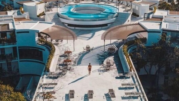 Une piscine sur le toit, dotée de chaises longues et d’un espace salon couvert, le tout entouré d’immeubles modernes.