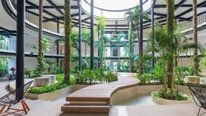 Un atrium à plusieurs niveaux, doté d’un escalier central, et entouré d’une végétation luxuriante et d’espaces de détente modernes.