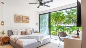 A modern bedroom with a bed, bedside tables, a desk, and a ceiling fan. - 104B PANOR, Modern Studio with 360° Pool-2 (Tulum)