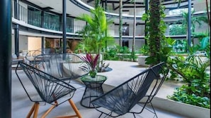 A multi-level atrium with modern architecture, featuring a central seating area with chairs and a table, surrounded by lush greenery and plants. - 105D PANOR, Large Studio with 360° Pool-2 (Tulum)