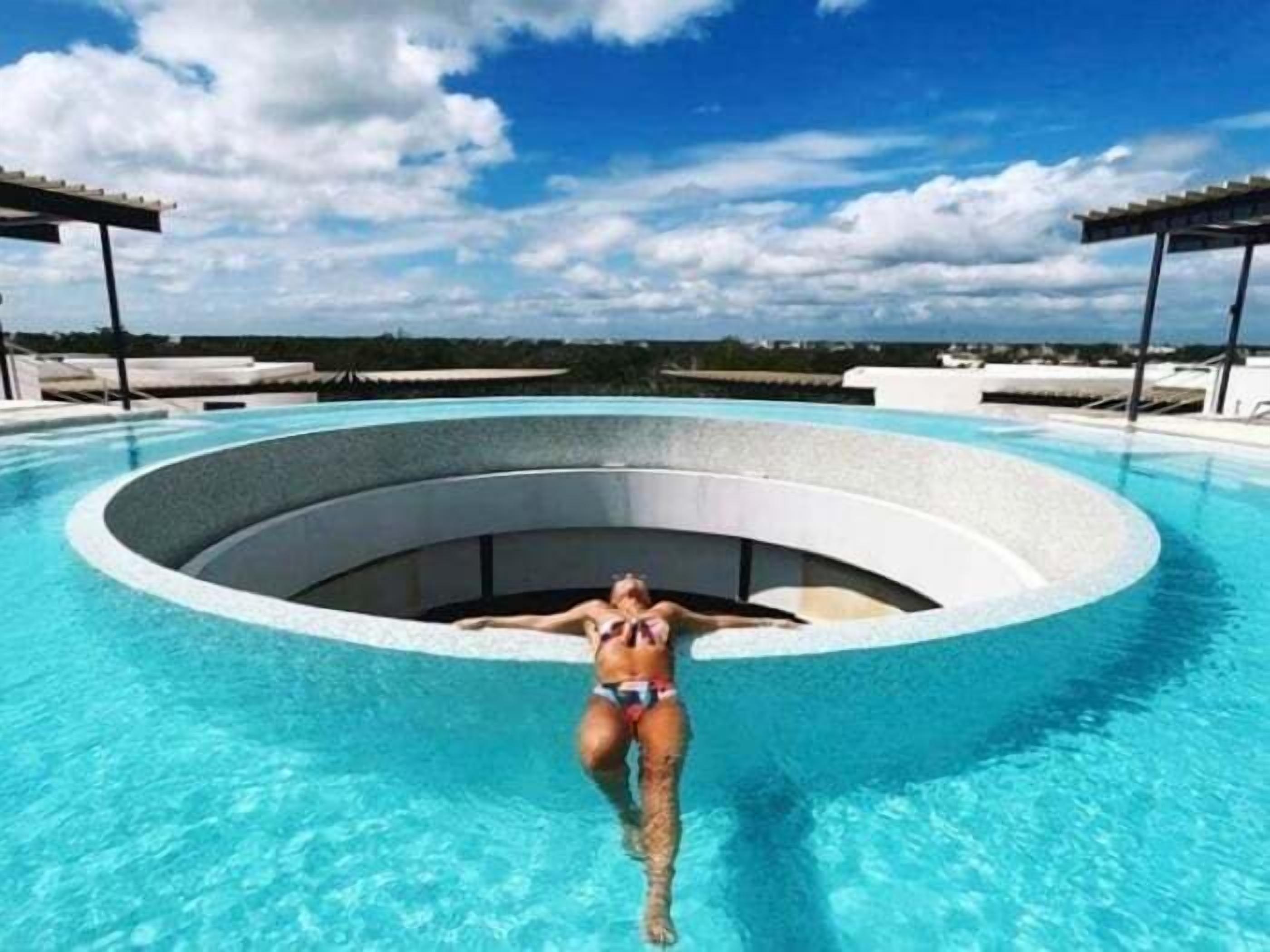 Uma piscina infinita circular com água azul cristalina, rodeada por um deck branco e uma estrutura de pérgula.