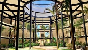 A multi-level atrium with a central glass dome, surrounded by palm trees and a water feature. - 204B PANOR, Charming Studio! 360° Pool-2 (Tulum)