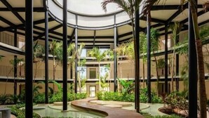 Un atrium à plusieurs niveaux, doté d’une passerelle centrale en bois, entouré d’une végétation luxuriante et agrémenté d’éléments aquatiques.
