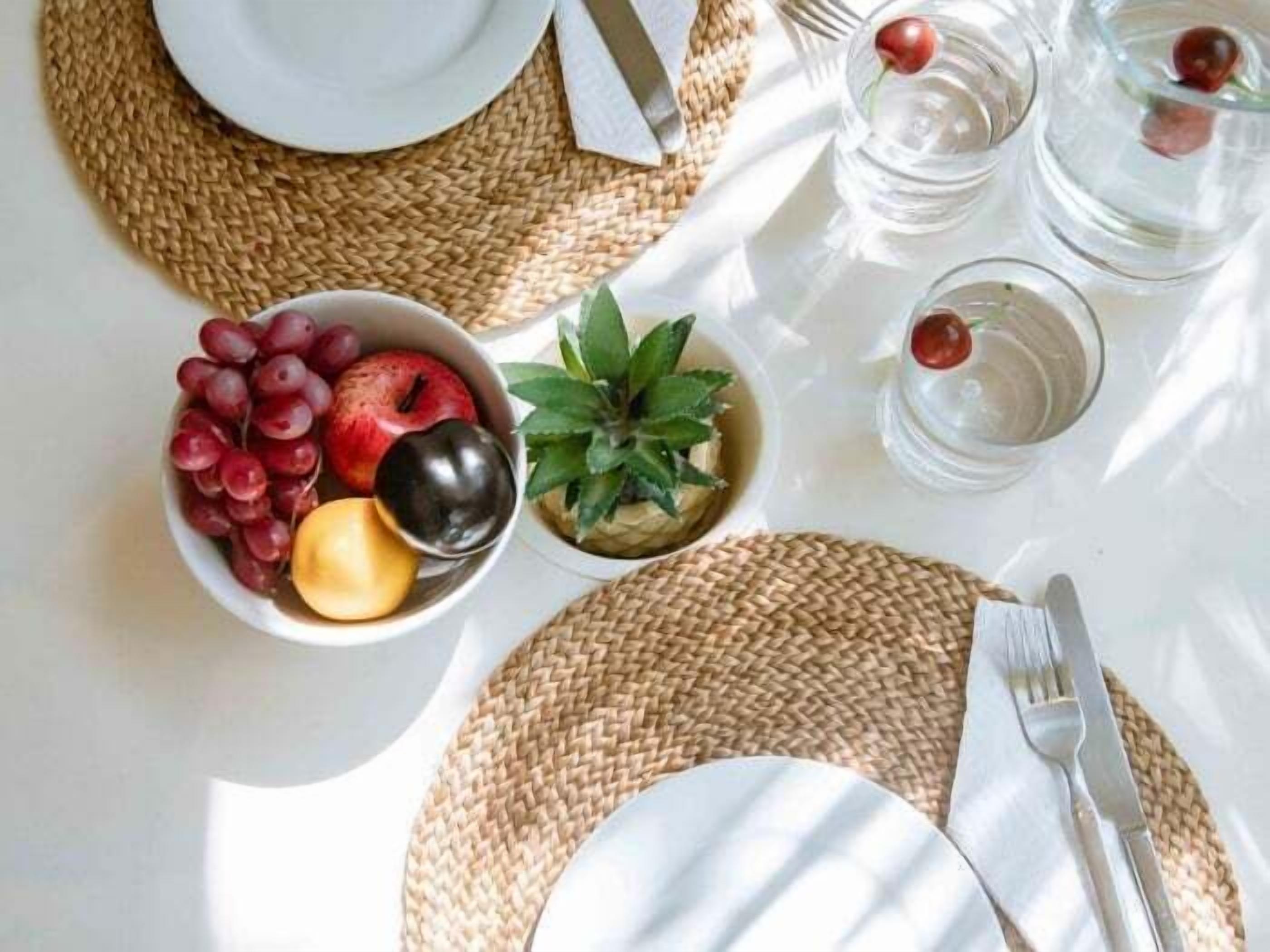 Een gedekte tafel met een schaal fruit, een glas water, een vork en mes.