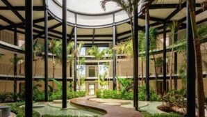 En fleretages atrium med et centralt vandelement, omgivet af frodigt grønt og moderne arkitektur.
