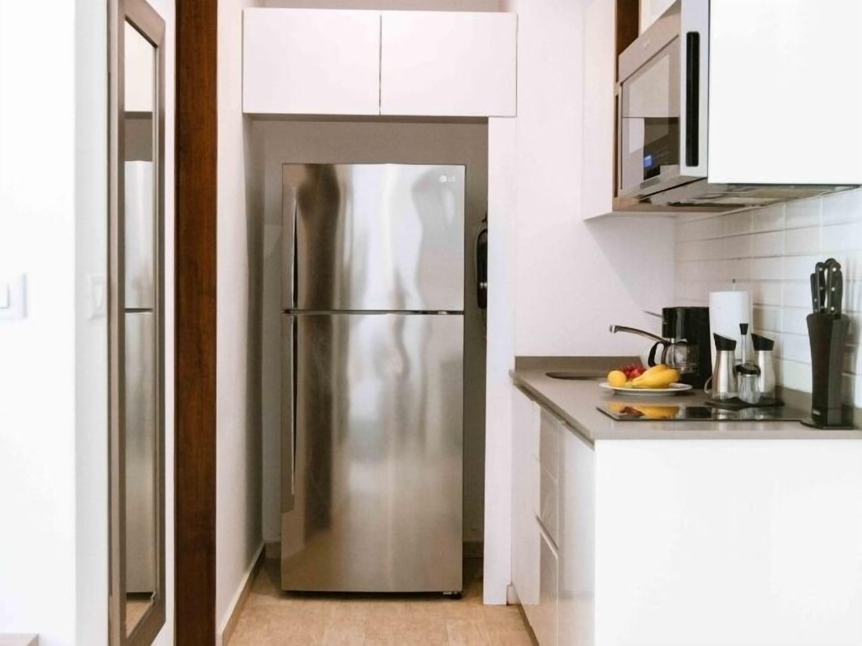 Una cocina moderna con un refrigerador de acero inoxidable, armarios blancos y una encimera con utensilios de cocina.